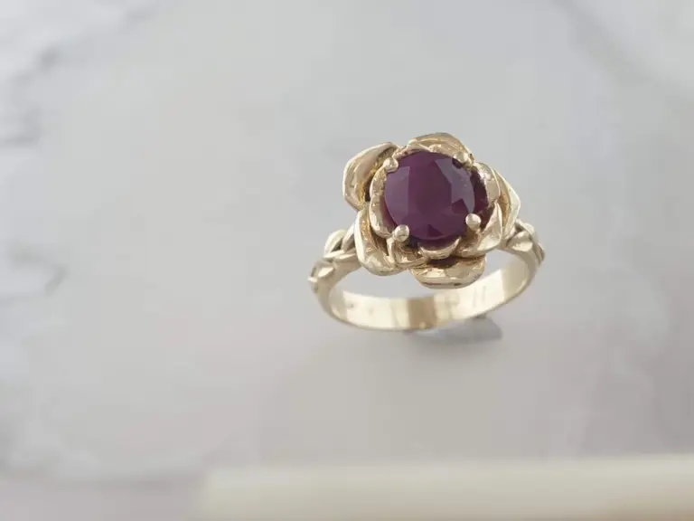 Gold ring with a large, round, deep purple gemstone set in a floral design.