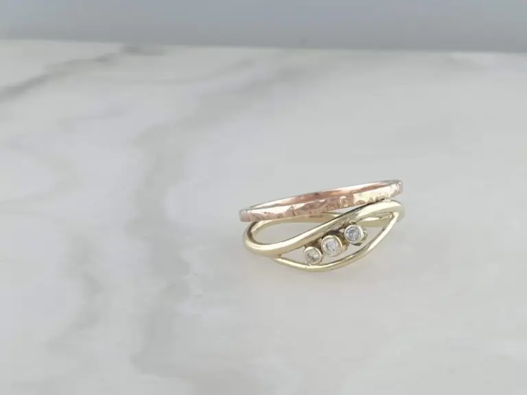 Close-up of multiple stacked rings with varying textures and small gemstones, on a light background.