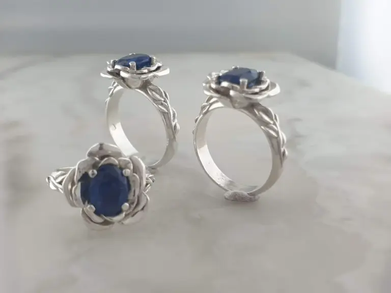 Silver rings with blue gemstones, intricately designed with flower petal patterns, displayed against a plain background.