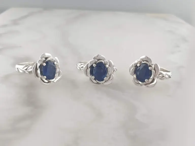 Three silver rings with oval blue gemstones, arranged in a horizontal line on a white surface.