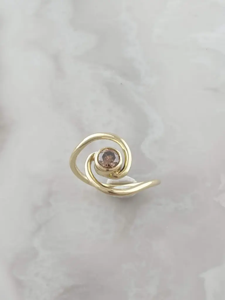 A gold ring with a spiral design and a central dark pink gemstone.