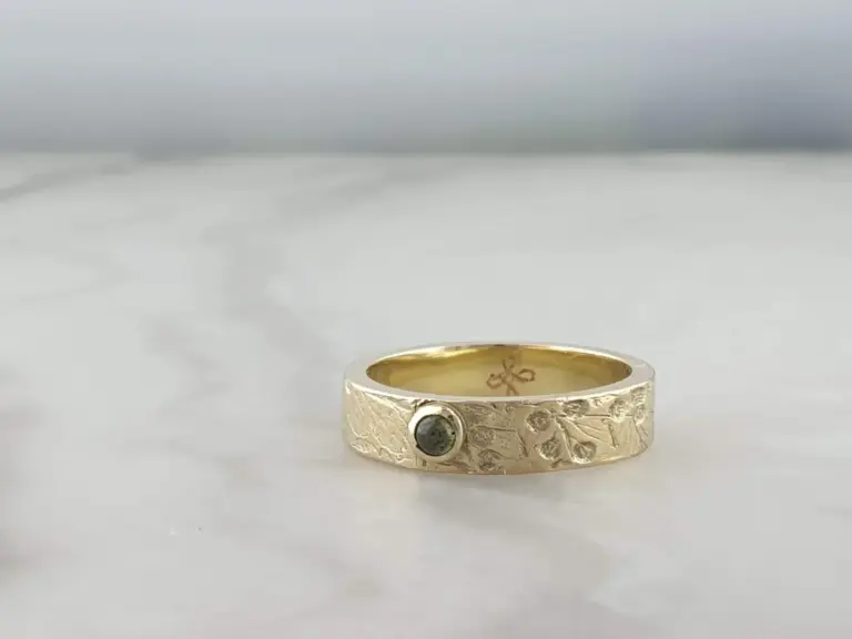 A gold ring with textured surface and two dark stones embedded, resting on a white surface.