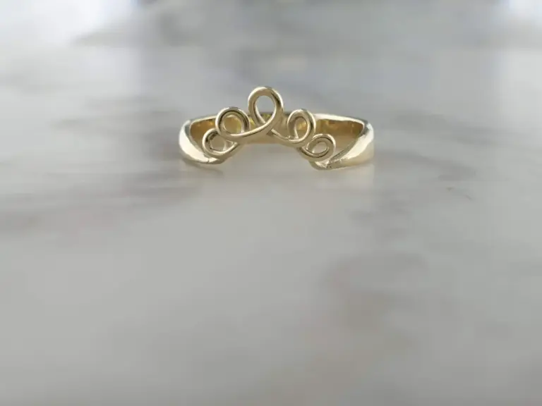 A gold ring with an intricate, curly design set against a plain background.