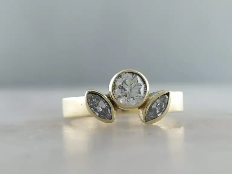 Close-up of a gold ring with a central large round diamond and four petal-shaped diamonds surrounding it on a light surface.