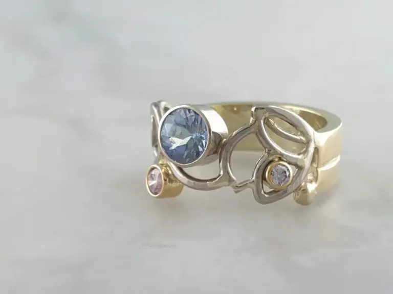 Multiple rings with embedded gemstones, including a large blue gemstone and smaller clear pink and white gemstones, set in gold and silver bands.