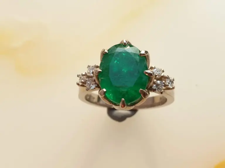 Close-up of a ring with a large oval green gemstone surrounded by smaller clear stones.