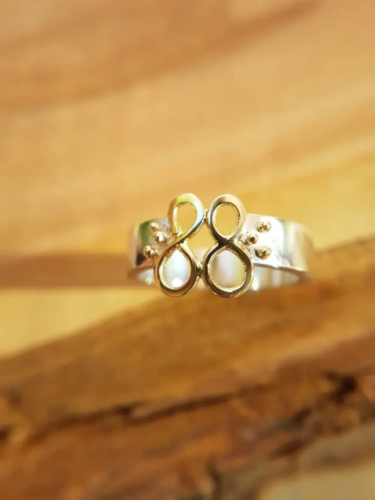 A gold ring with a decorative design featuring the number 20 and small spheres, resting on a wooden surface.
