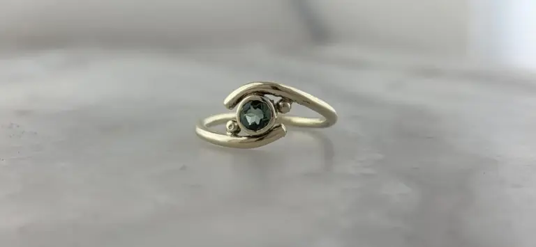 A silver ring with a round, dark gemstone in the center, resting on a white surface.