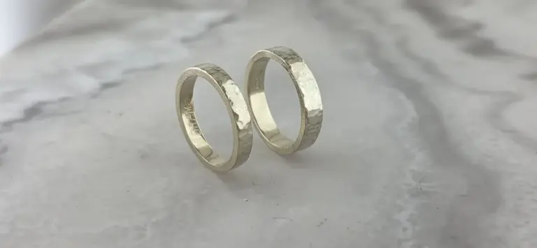 Two silver textured wedding rings placed on a smooth white surface.
