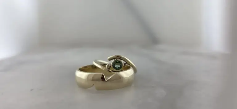 Close-up of a gold ring with a green gemstone on a light gray surface.