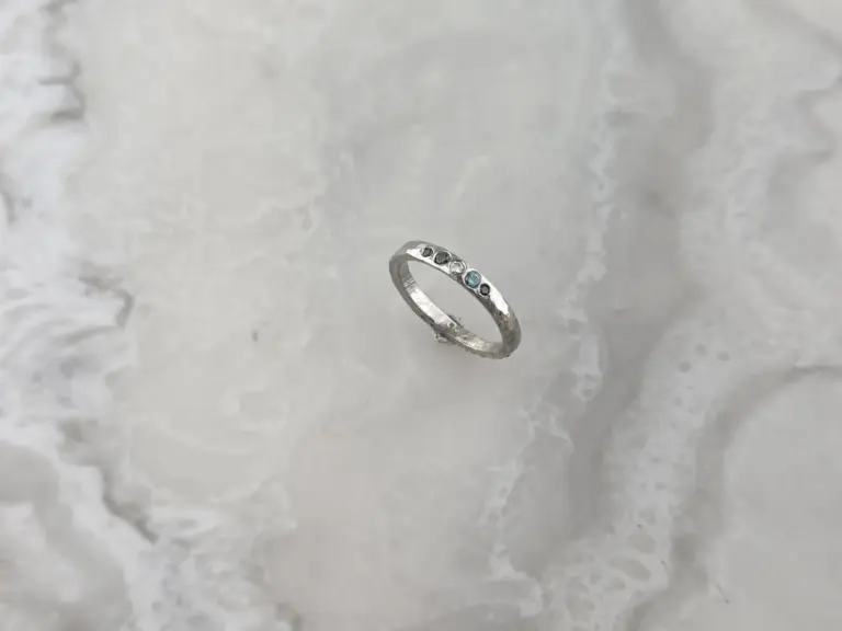 A silver ring with multiple small gemstones set around the band, positioned on a marble surface.