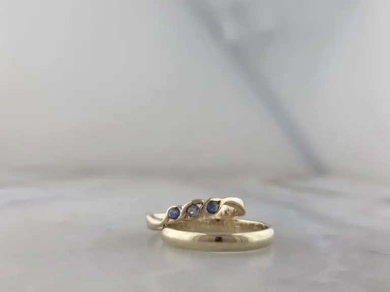 A gold ring with three blue gemstones and one clear gemstone set into the band, resting on a white surface.