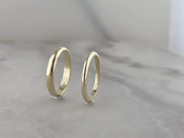 Close-up of two silver wedding bands standing upright on a plain surface.