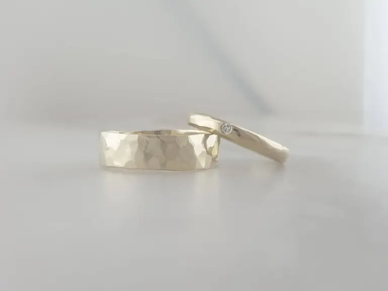 Two silver rings with textured surfaces, one with a small gemstone, placed on a reflective white surface.