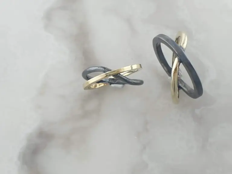 Close-up of intertwined black and gold rings on a white surface.