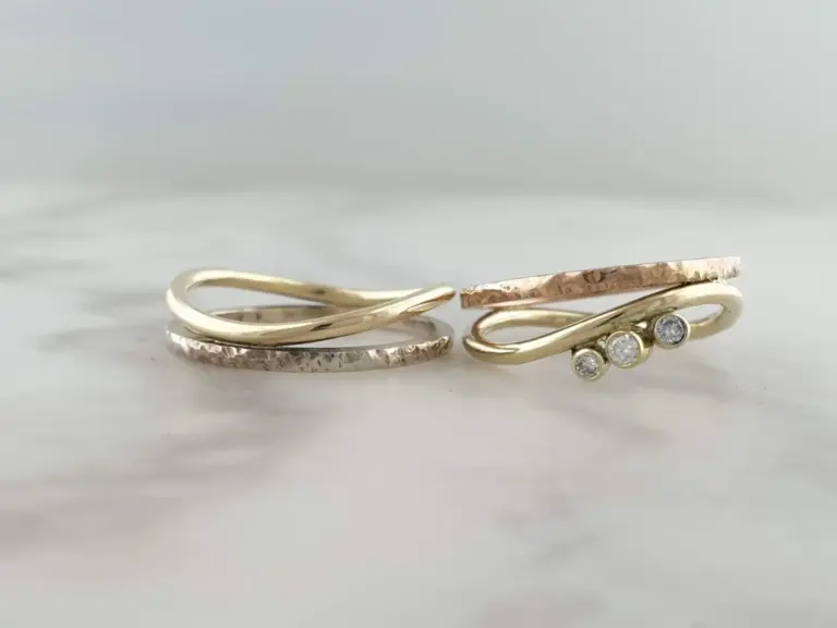 Three gold rings with different designs, one with diamonds, arranged on a white surface.