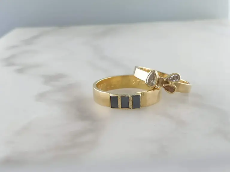 Close-up of two gold rings with embedded diamonds, resting on a soft, light-colored surface.