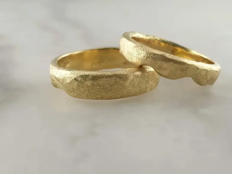 Close-up of two gold wedding bands with textured surface on white background.