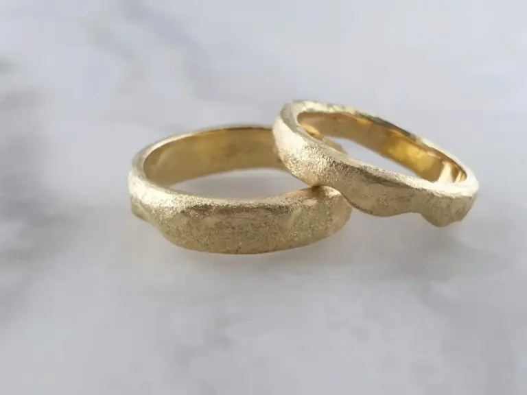 Two gold wedding bands with rough textured surfaces on a white background.
