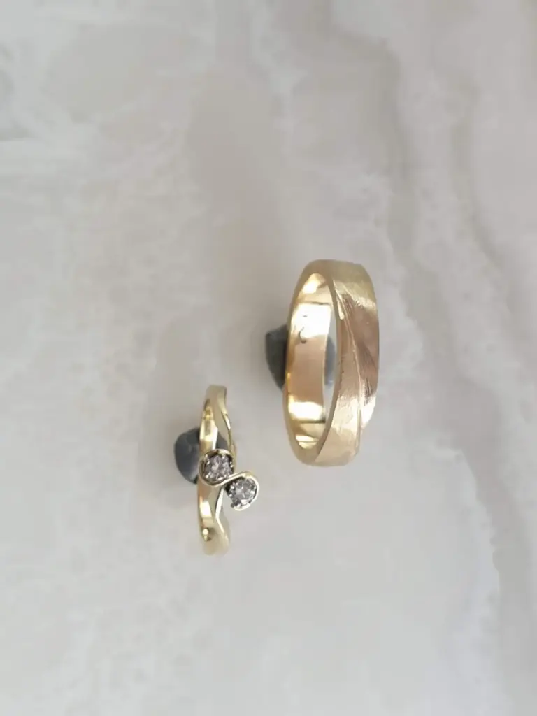Close-up of three rings, one with a brushed gold finish and the others with gemstones, on a light gray background.