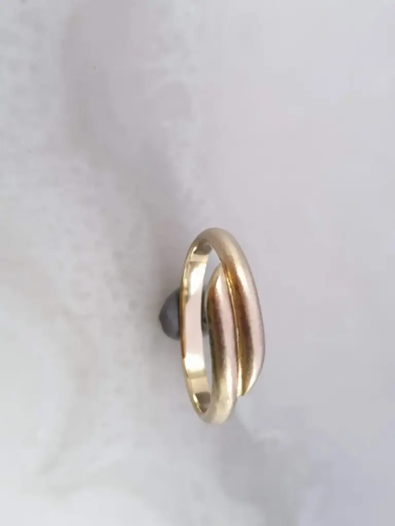 Two gold rings stacked together on a white surface with a dark smooth oval object behind them.