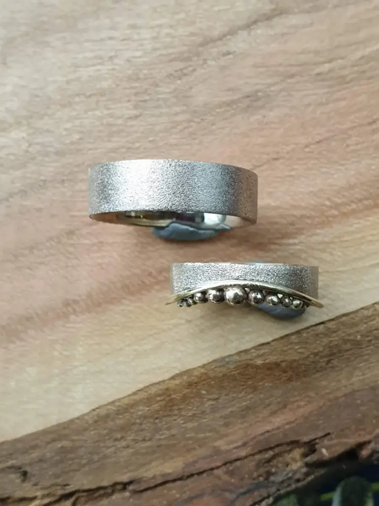 Close-up of two silver rings on a wooden surface, one with a textured matte finish and the other with small beads along its band.
