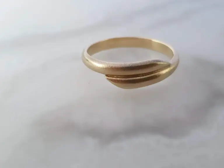 A close-up of a simple, plain gold ring placed on a white surface with a shadow cast on the background.