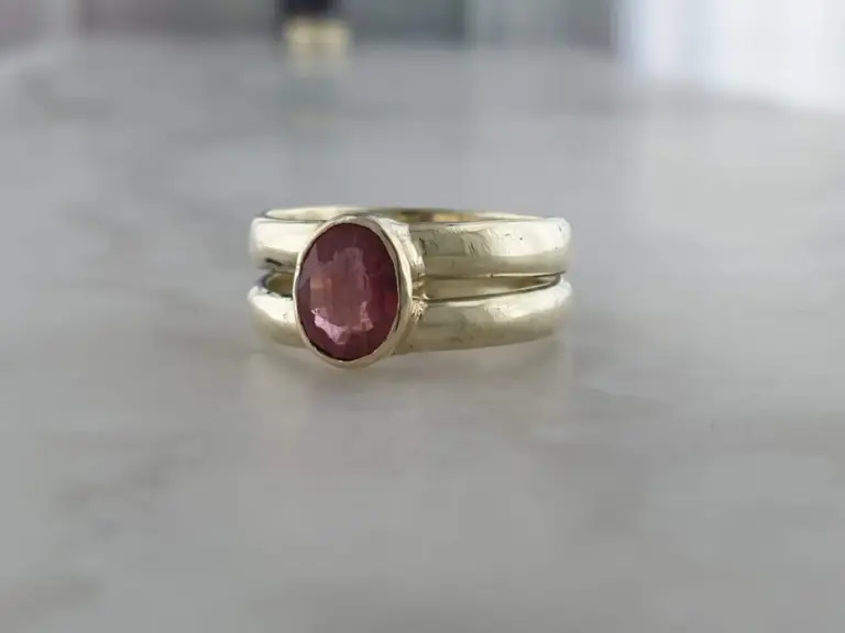 Close-up of a silver ring with an oval-shaped pink gemstone set in the center, resting on a smooth, reflective surface.