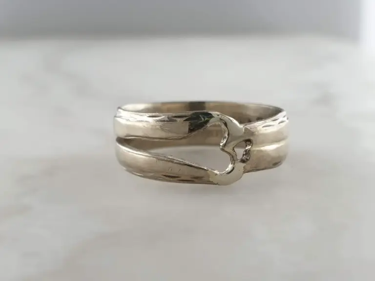 Close-up of a silver ring with an abstract organic design, placed on a white surface with a soft gray background.