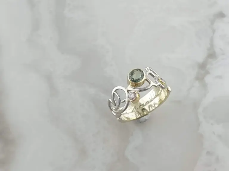 Close-up of a mixed metal ring with gemstones on a reflective marble surface.