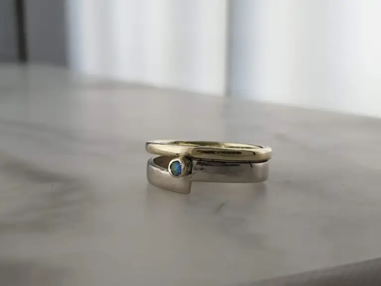 Close-up of two silver rings stacked together, with one featuring a small blue gemstone, placed on a white surface with a blurred background.