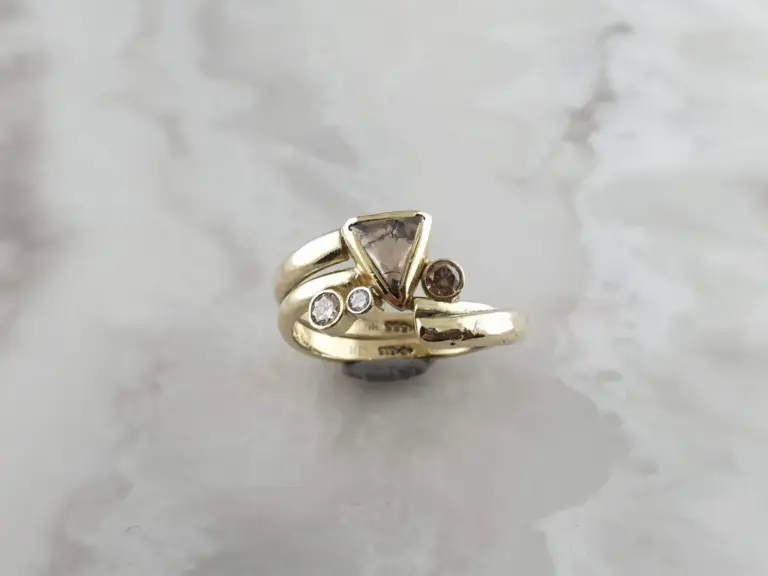 Close-up of gold rings with diamonds and a triangular gemstone on a gray marble surface.