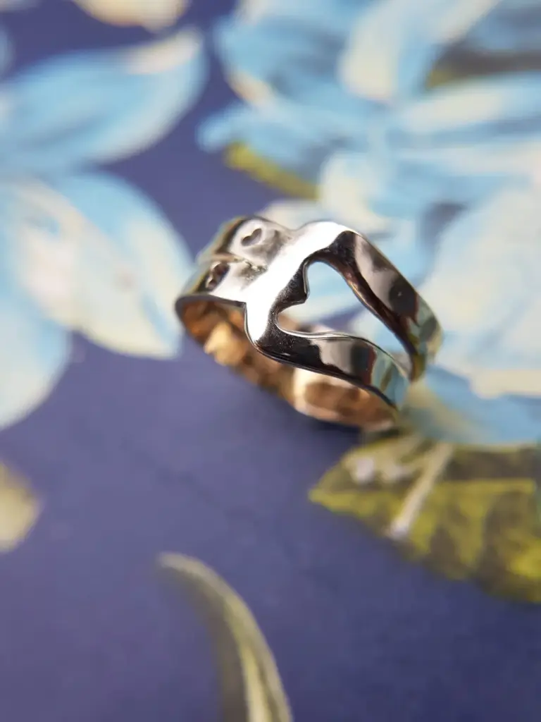 Close-up of a silver ring with a smooth, shiny surface placed on a blurry background with blue, white, and yellow colors.