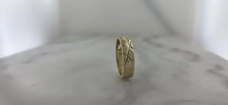A silver ring with a carved geometric pattern, standing upright on a white surface against a plain background.