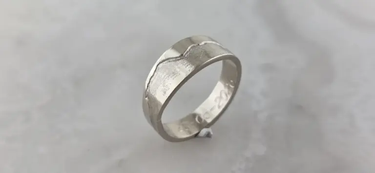 Close-up of a silver ring with engraved text and a textured design on a gray background.