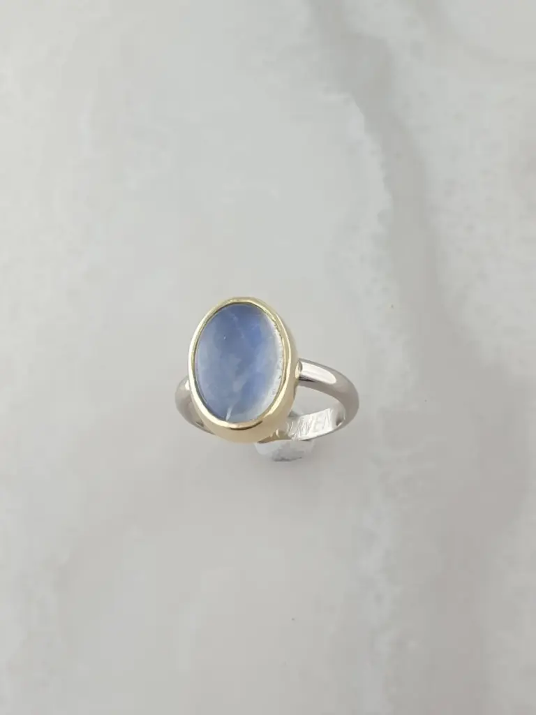 A ring with a large oval-shaped blue gemstone in a gold setting and a silver band engraved with the word 'FLOWER'.