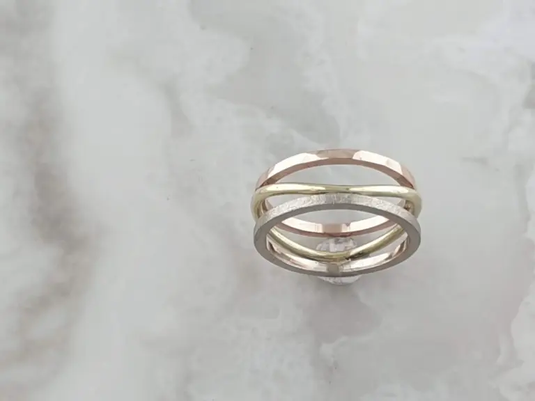 Close-up photo of multiple stacked rings in different colors, including pink, yellow, and silver, on a light gray surface.