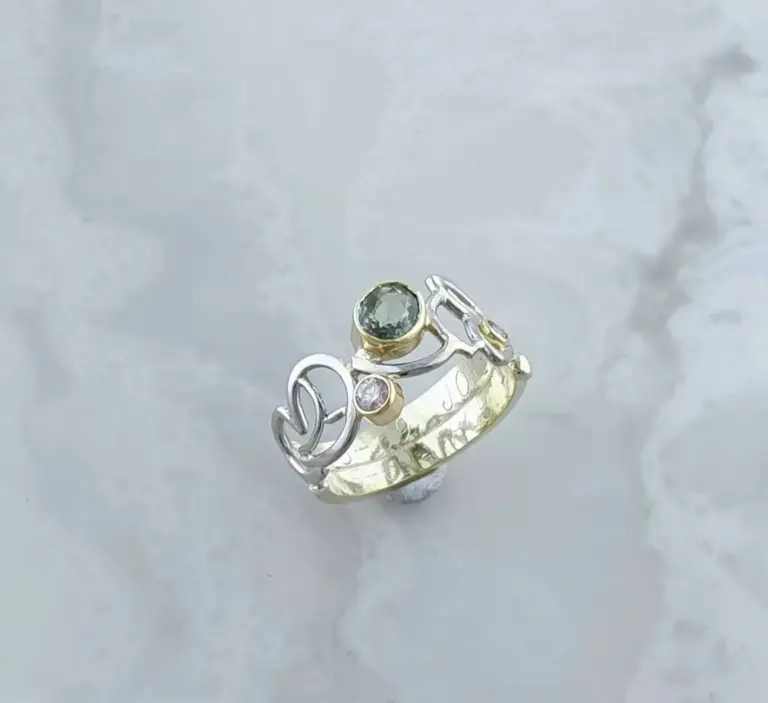 A silver ring with intricate design and embedded gemstones resting on a reflective, textured surface.