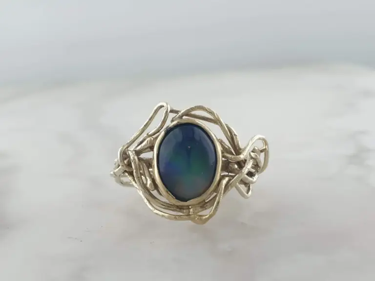 Silver ring with a large, round, deep blue gemstone in a silver setting with intricate, swirling silver details around it.