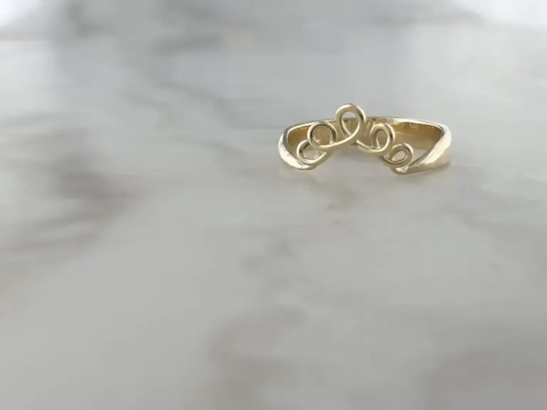 Close-up of a gold ring with a decorative swirl design, resting on a reflective surface.