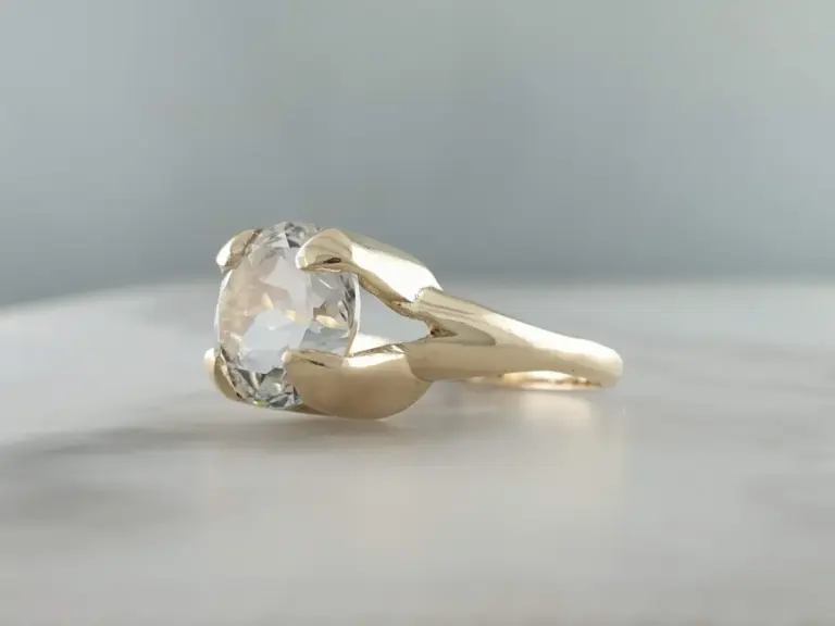 Close-up of a silver ring with a large, faceted clear gemstone, held by a hand with a gray background.